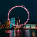 Photo of Luminous Ferris Wheel in Modern City District on River Bank at Night